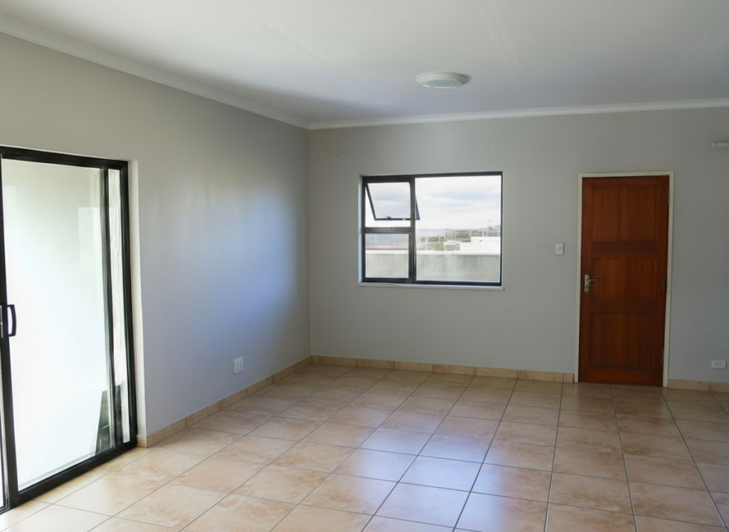 Spacious living room in the Crystal Park development featuring beige floor tiles, aluminium sliding door, grey walls and natural light – Kwantu Homes.