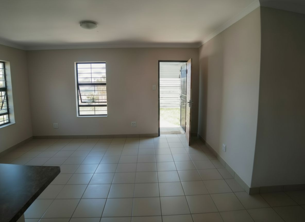 Open-plan living and dining area in the Crystal Park development, featuring tiled floors, aluminium windows, and a front door opening to the garden.