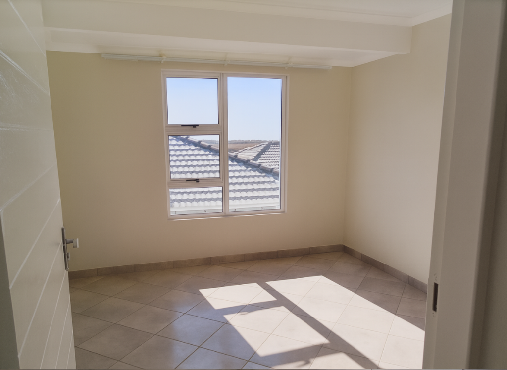 Bright bedroom at Greenwood Gardens with tiled floors and natural light through large windows.