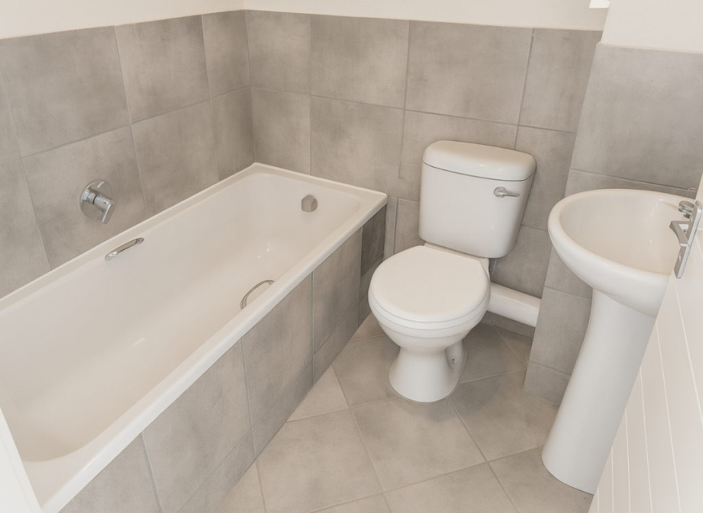 Modern bathroom at Greenwood Gardens with built-in bath, toilet and pedestal basin, finished in large grey tiles.