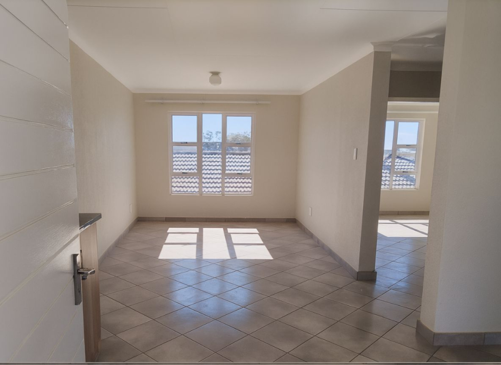 Open-plan living area at Greenwood Gardens with tiled floors and large windows bringing in natural light.