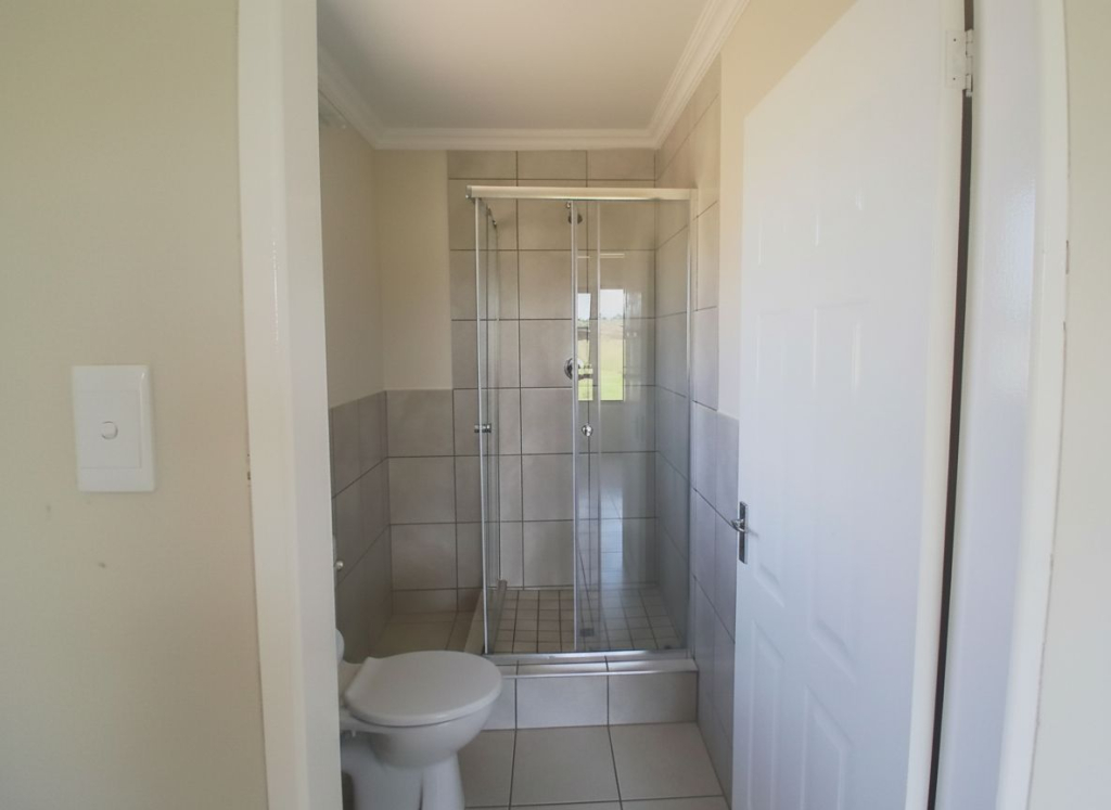 Modern tiled bathroom in the Selcourt development featuring a glass shower, toilet, and neutral wall finishes.