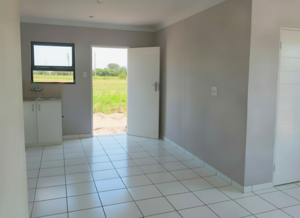 Entry area of a Selcourt home with tiled floors, light grey walls, an open front door, and a compact kitchenette with a window.