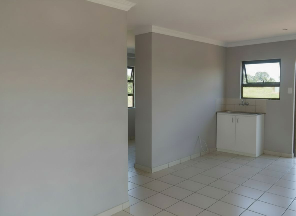 Open-plan living area in a Selcourt home showing tiled floors, neutral grey walls, and a compact kitchenette with a window.