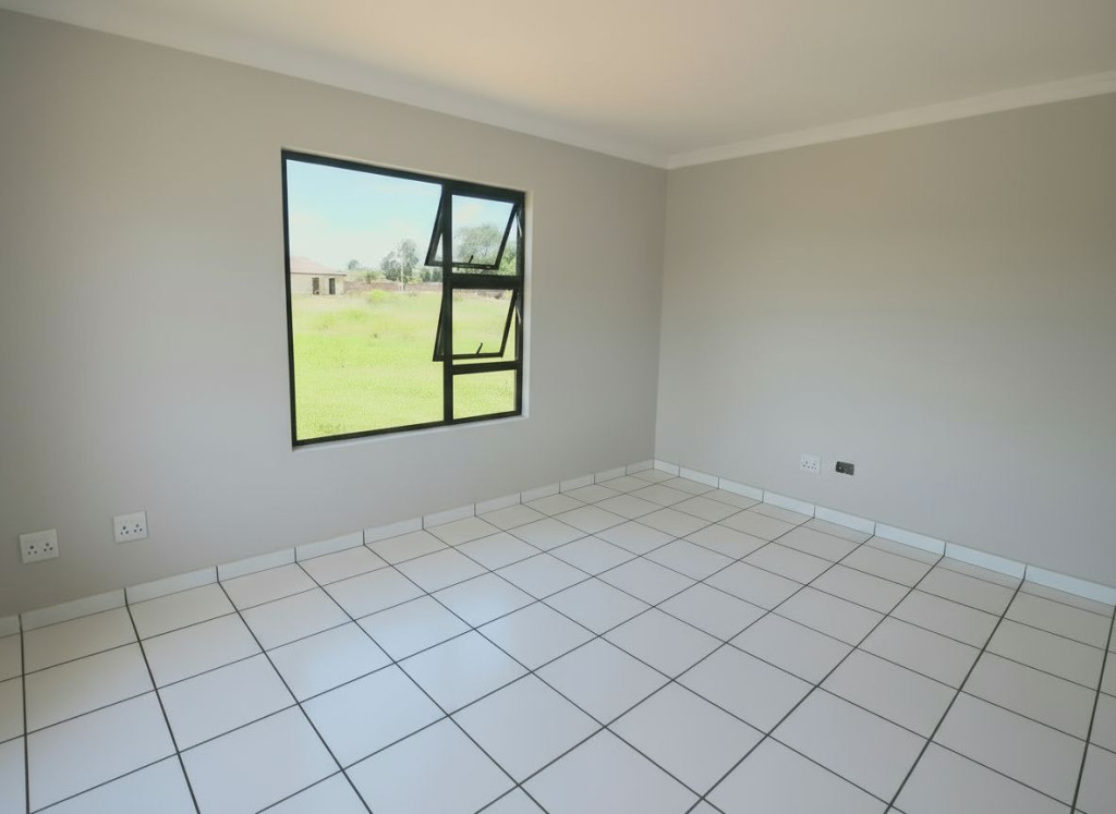 Bedroom interior of a Selcourt home featuring white tiled floors, light grey walls, and a large window overlooking open green space.