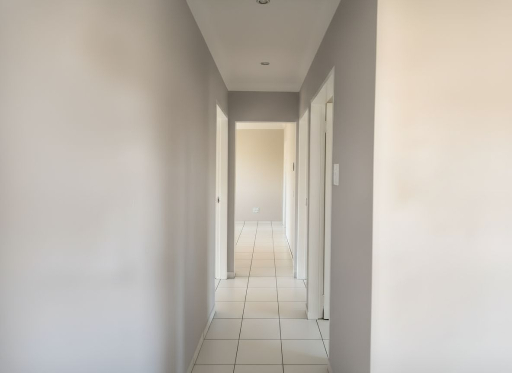 Interior passage of a Selcourt home with white tiled flooring, soft grey walls, and doorways leading to bedrooms and bathroom.